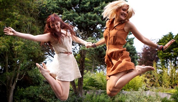 Фотография двух молодых женщин, прыгающих, держась за руки