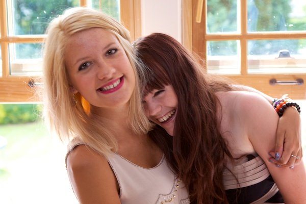 Фотография двух молодых женщин, одна из которых обнимает другую, которая смеется