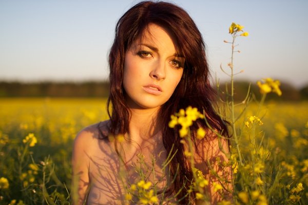 Фотография молодой женщины в поле желтых цветов, смотрящей в камеру