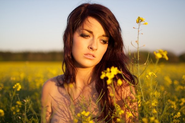Фотография молодой женщины в поле желтых цветов, смотрящей вниз