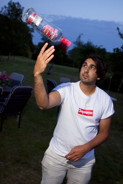 Мужчина жонглирует бутылкой водки на улице при слабом освещении - фотосъемка вечеринки