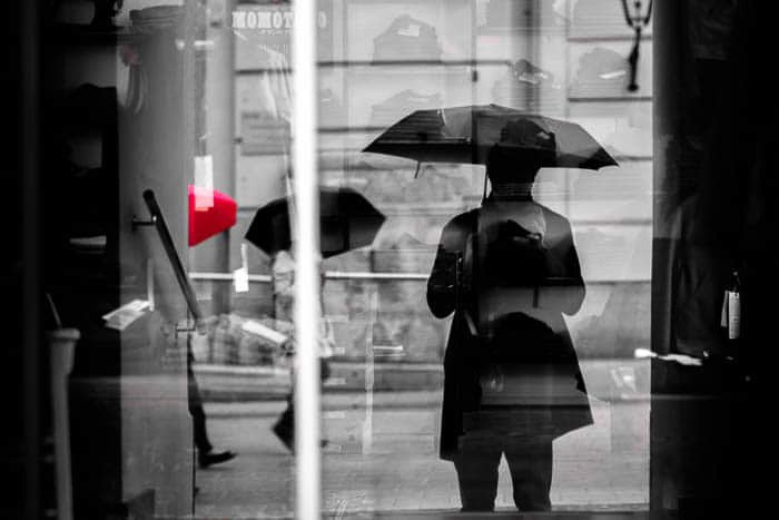 Черно-белая уличная фотография людей, идущих под дождем, один зонт окрашен в красный цвет