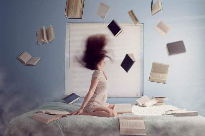 Концептуальный портрет девочки в ее спальне в окружении летающих книг