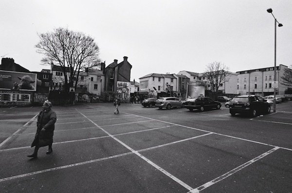 Женщина идет перед машинами на парковке - черно-белая уличная фотография