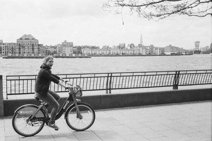 Черно-белый снимок девушки, проезжающей на велосипеде мимо реки, сделанный винтажной камерой Rollei B35