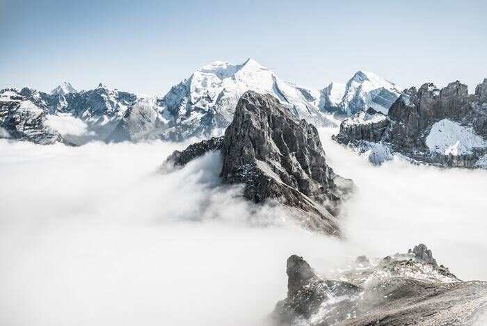 Фотография высокого горного пика с облаками вокруг него