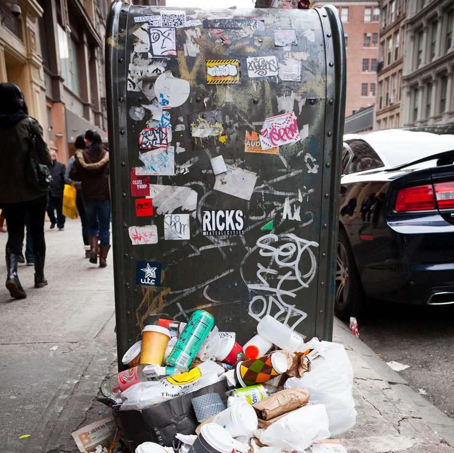 Уличная фотография: Почтовый ящик, покрытый граффити и наклейками, с кучей мусора на переднем плане