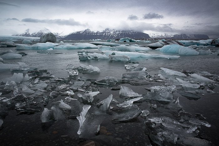 пейзажная фотография ледяной реки с плавающими в ней замороженными кусками льда и горами вдали, сделанная в Исландии