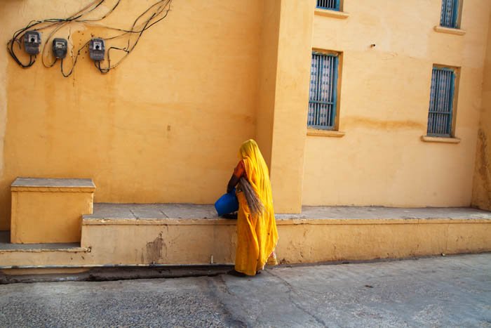 использование цвета в композиции уличной фотографии, на фотографии изображена женщина в желтой одежде, стоящая спиной к камере, лицом к желтой стене здания