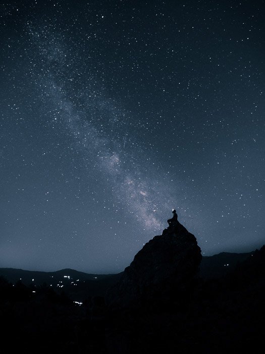 Потрясающий снимок астрофотографии звездного неба над силуэтом человека на скале