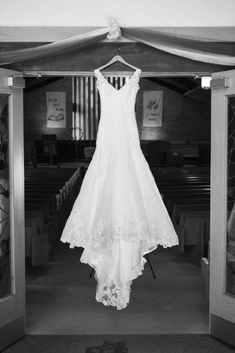 Черно-белая свадебная фотография свадебного платья, висящего над дверями церкви