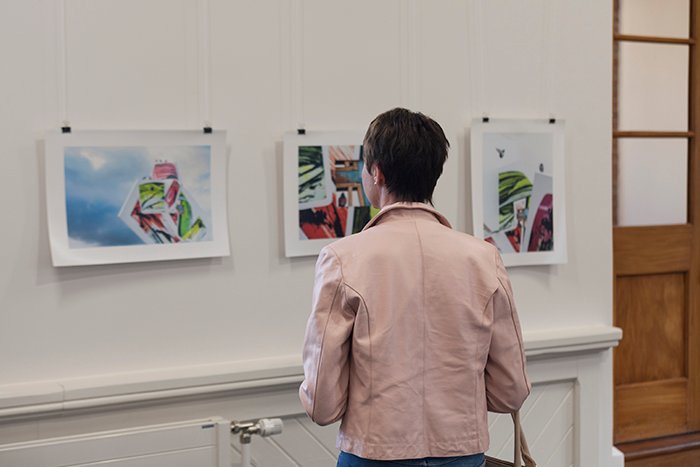 женщина в розовом пиджаке рассматривает картины на художественной выставке