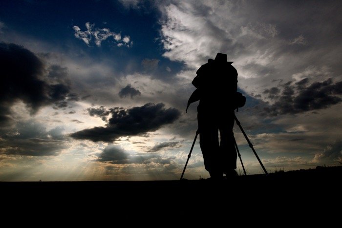 силуэт фотографа, снимающего пейзаж на штативе