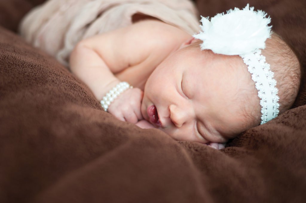 крупный план портрета новорожденного ребенка на коричневом материале, в жемчужной повязке и браслете. фотография новорожденных