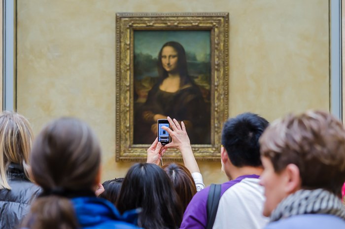 Толпа перед картиной Мона Лиза, пока один из туристов делает снимок на свой смартфон