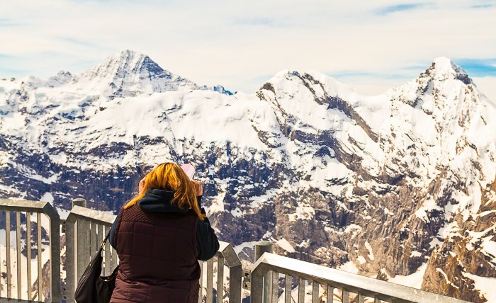 фотография девушки, смотрящей со смотровой площадки на заснеженные скалистые горы