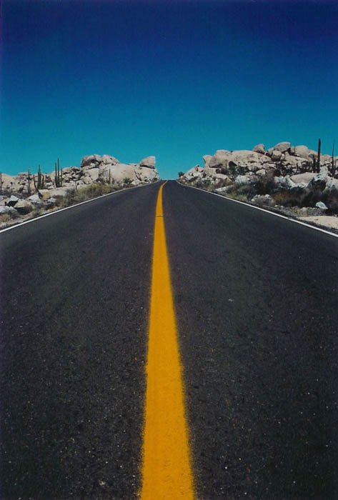 Фотография шоссе, уходящего в горизонт, голубое небо и желтая полосатая дорога