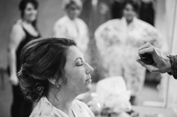 черно-белая свадебная фотография невесты, делающей макияж, с подружками невесты на заднем плане