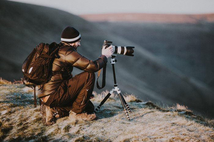 изображение мужчины в горах, устанавливающего камеру с телеобъективом на штатив