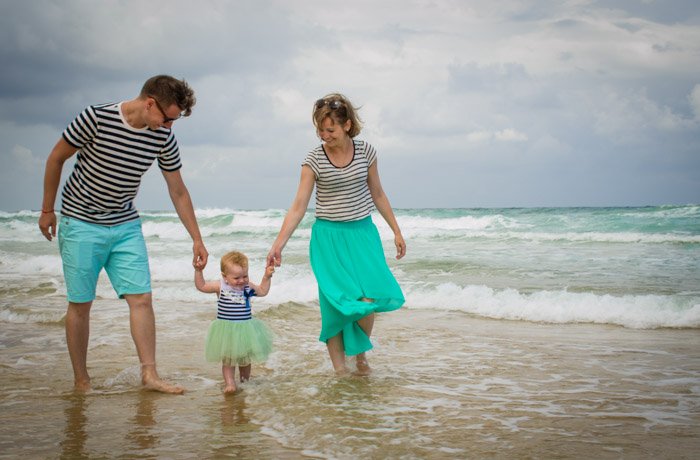 семейная фотография пары и маленького ребенка, гуляющих по пляжу