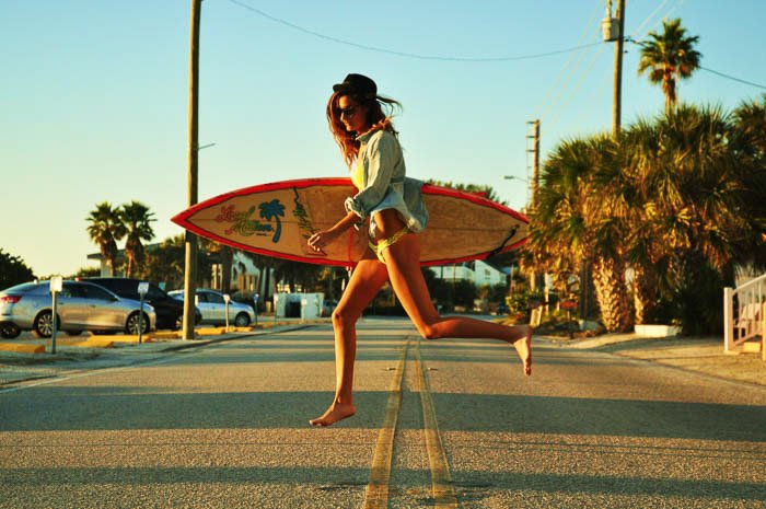 Модная фотография женской модели, идущей с доской для серфинга
