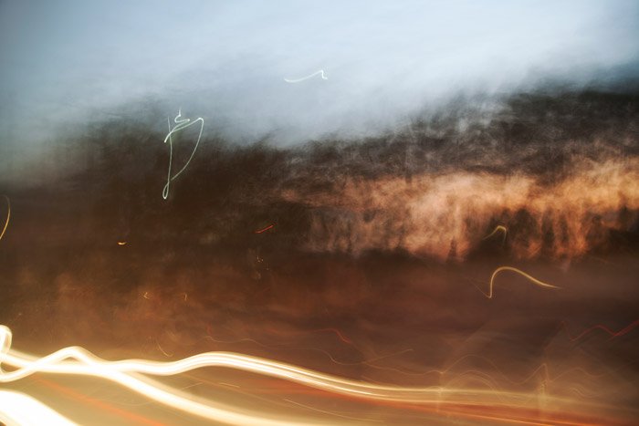 Фотография размытых светлых следов и кустов, сделанная во время поездки по шоссе в сумерках. Идеи абстрактной фотографии.