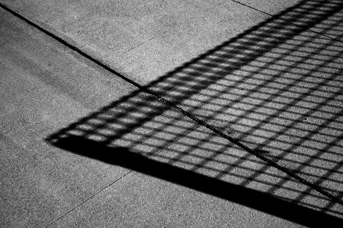 Черно-белая фотография тени от забора из проволочной сетки на бетоне. Идеи абстрактной фотографии.