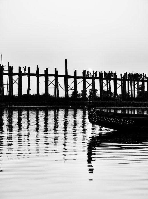 Черно-белая туристическая фотография моста У-Бейн в Мьянме, мост и лодка красиво отражаются в воде