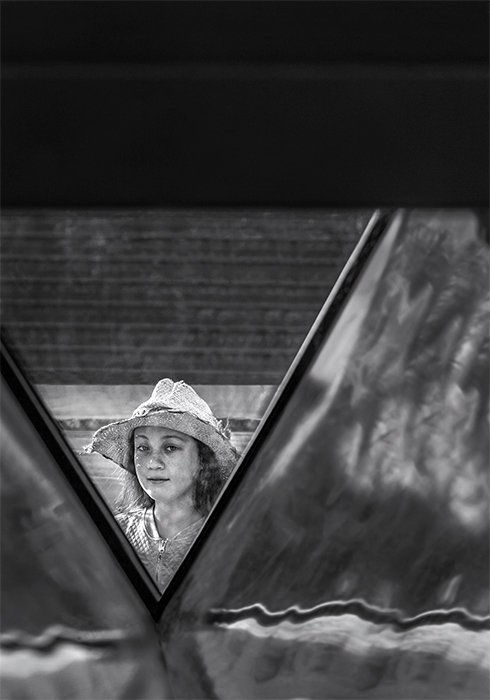Черно-белая фотография девушки в белой шляпе в обрамлении архитектурных деталей. Креативная уличная фотография