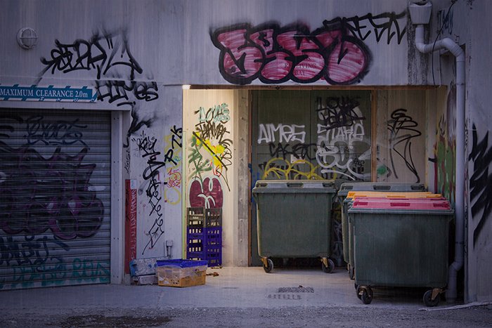 Креативная уличная фотография зданий с граффити и мусорными баками.