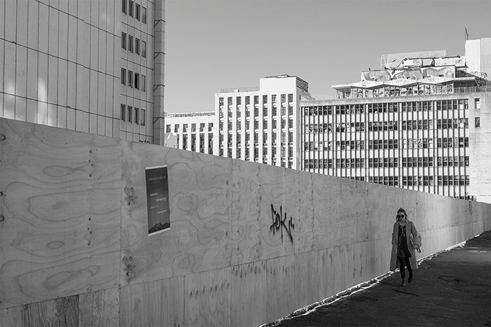 Черно-белая уличная фотография городского рабочего, проходящего мимо пустой строительной площадки. Креативная уличная фотография