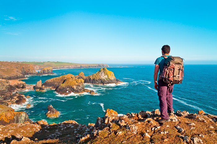 Мужчина-рюкзачник стоит на скалистых утесах с видом на фантастический морской пейзаж