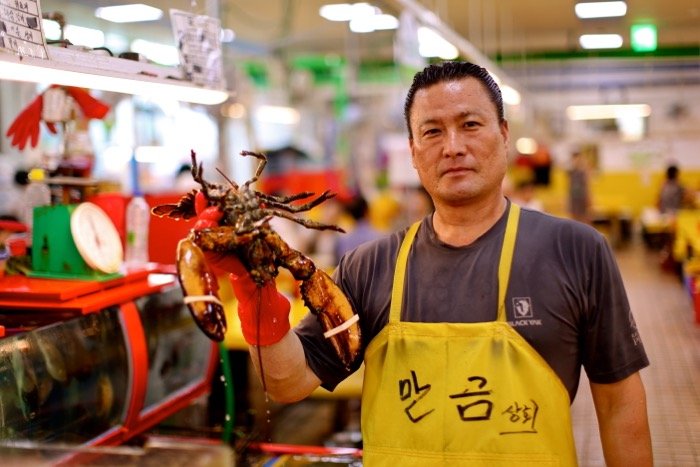 Портрет мужчины на рыбном рынке, держащего лобстера. 