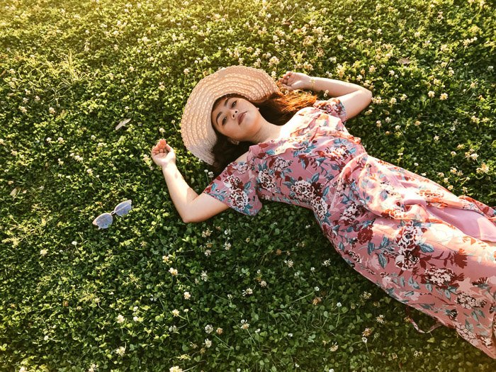 Девушка в розовом цветочном платье и соломенной шляпе лежит спиной на траве в яркий день - модная фотосессия на смартфон