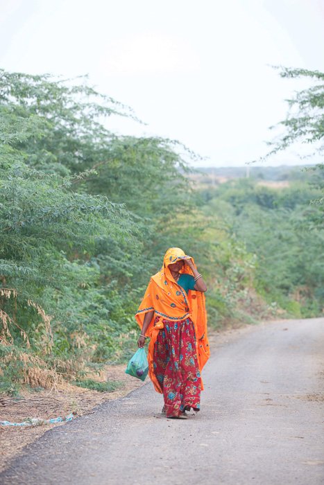 Тревел-фотография женщины в оранжево-красной одежде, идущей по спуску в Индии. 
