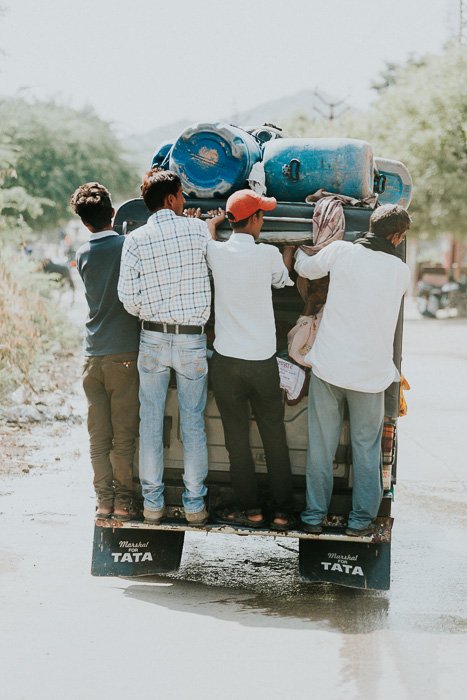 Туристическая фотография группы мужчин, держащихся за заднюю часть трейлера в Индии.