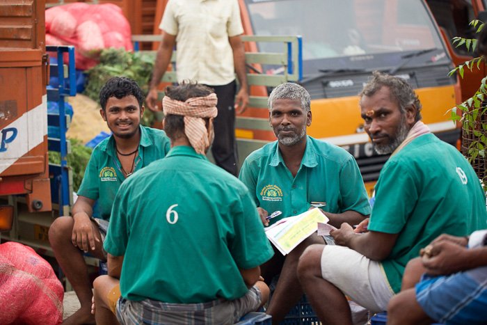 Тревел-фотография 4 мужчин в зеленом, сидящих на цветочном рынке в Индии. 