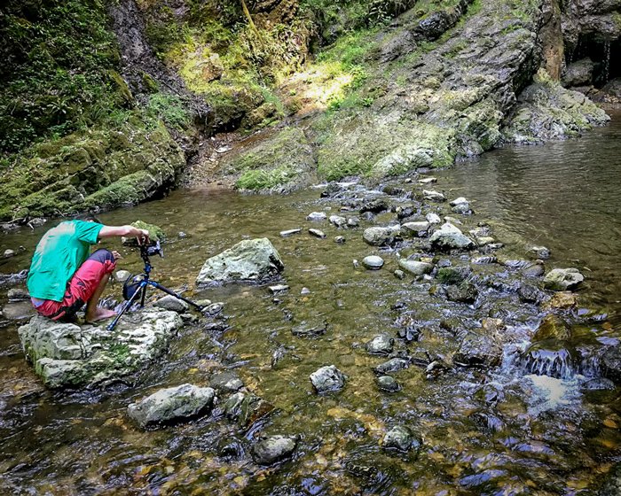 Фотограф сидит на скале со штативом и камерой, чтобы сделать снимки водопада