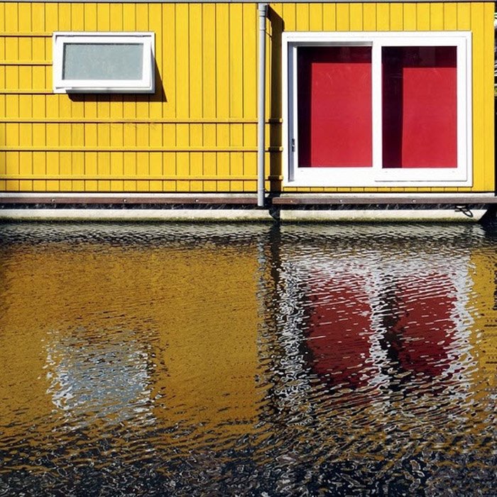 Фотография желтого дома с красными окнами, отражающегося в воде внизу
