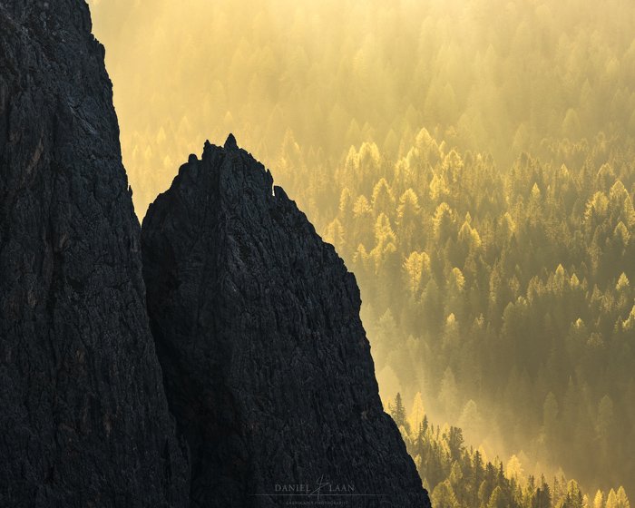 Художественная пейзажная фотография скалистой горы на фоне блестящего желто-зеленого леса.