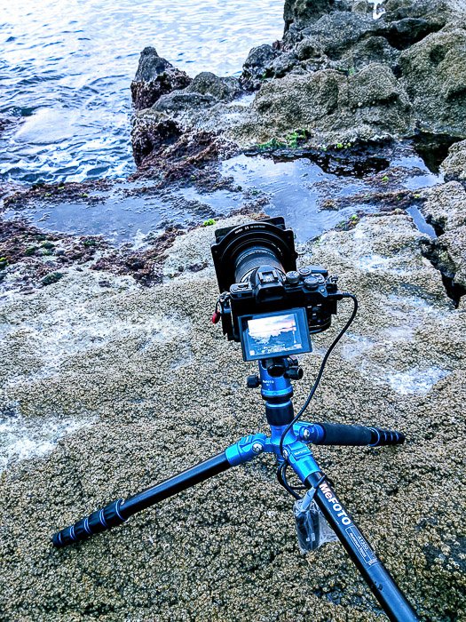 Изображение камеры и штатива, установленных на прибрежных скалах для съемки с длинной выдержкой. 