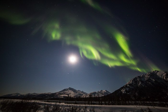 Фотография луны, освещающей теплым светом хребет Брукс на севере Аляски с авророй бореалис наверху. 