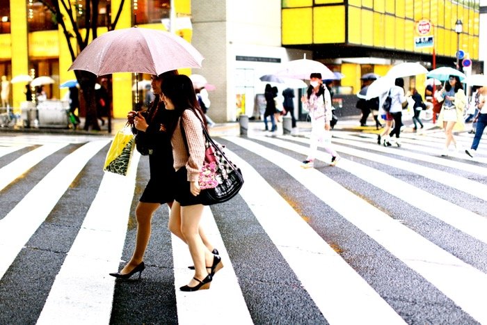 Дорожная фотография двух женщин с зонтиками, переходящих улицу, фон оживленной уличной сцены. 