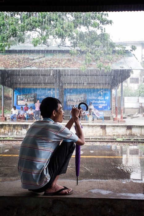 Тревел-фотография мужчины с зонтом, укрывающегося от тропического ливня. 