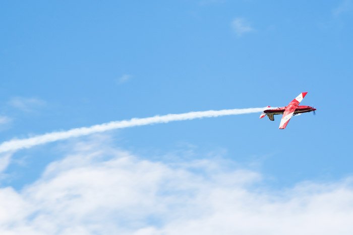 Снимок с авиашоу, на котором изображен красный самолет, летящий с потоком контраилов позади
