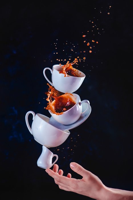 Фотография натюрморта балансирующих чашек с брызгами кофе на темном фоне - креативные идеи фотографии