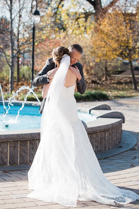 Sweet wedding day moment of a bride hugging her father in front of a fountain 