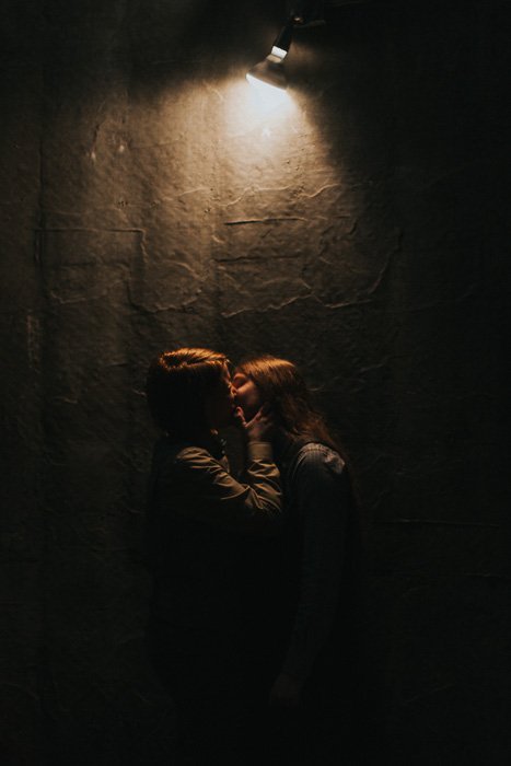 Пара целуется перед текстурированной стеной с единственным источником света