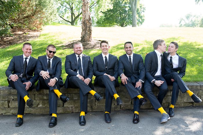 Юмористическая свадебная фотография семи женихов, сидящих на стене, все в желтых носках