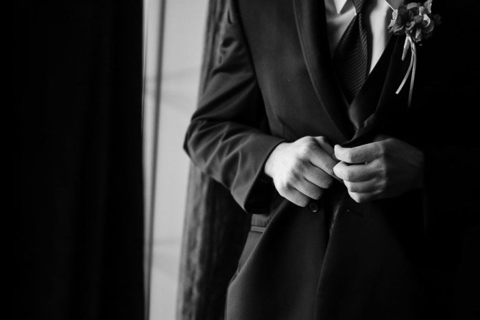 Черно-белая свадебная фотография жениха, застегивающего пиджак, крупным планом. Свадебная фотосъемка 